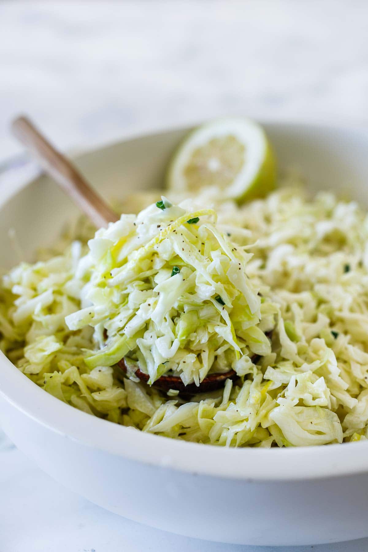 bowl of creamy coleslaw with wood spoon holding up a spoonful. 