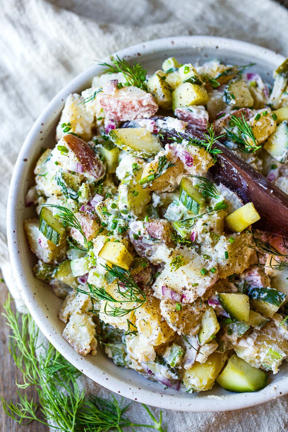 Creamy potato salad in a white bowl with a wooden spoon.
