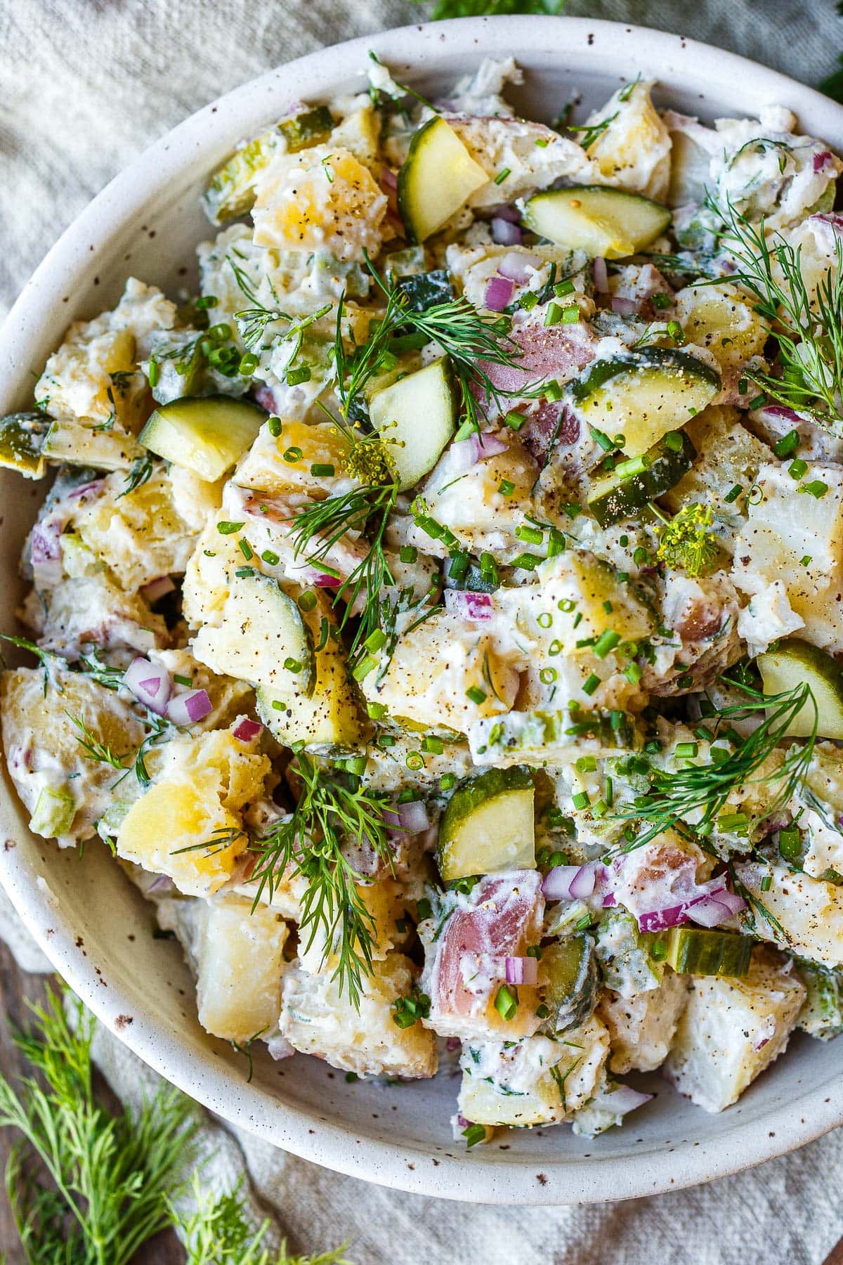Light and creamy potato salad recipe with quick pickled cucumbers, fresh dill, and yogurt dressing in a white bowl.