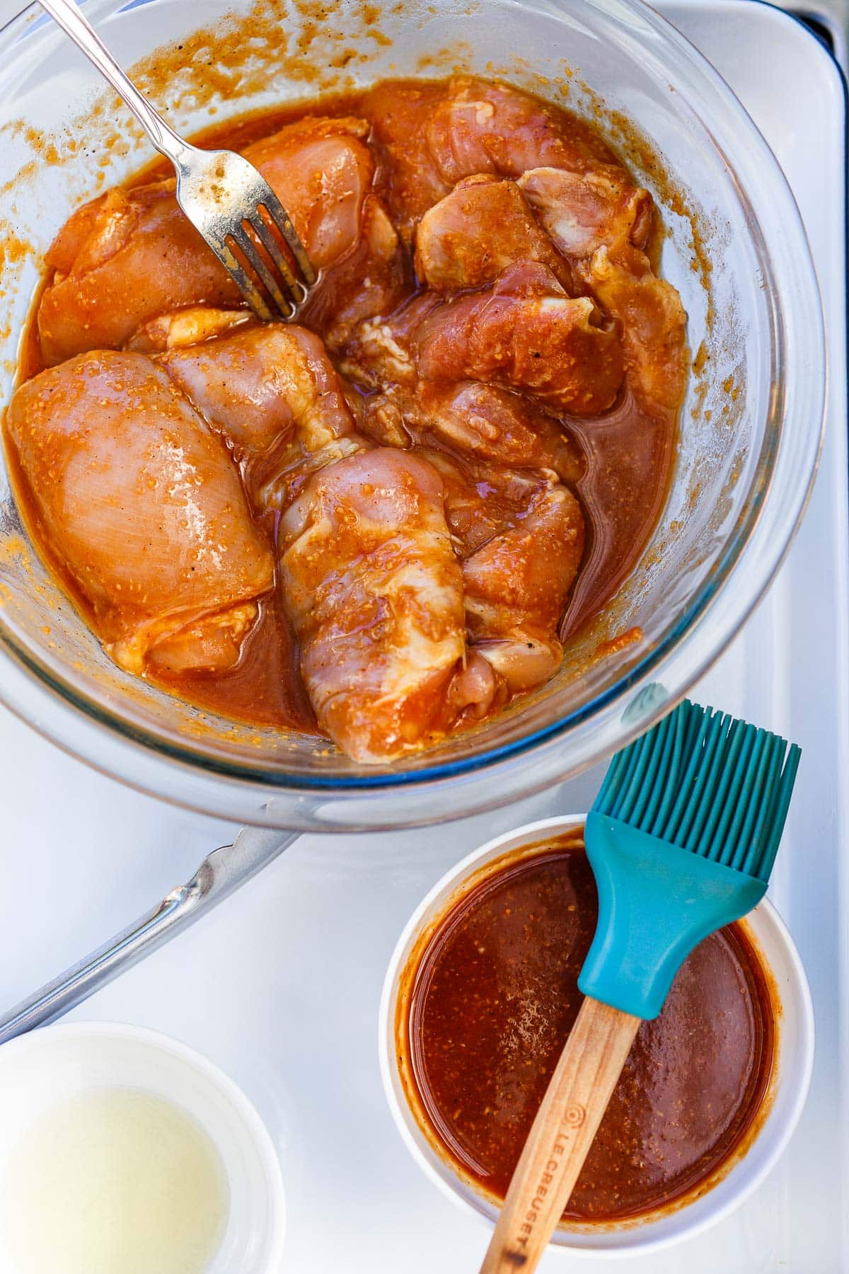 bowl of chicken thighs in huli huli marinade next to reserved marinade with brush.