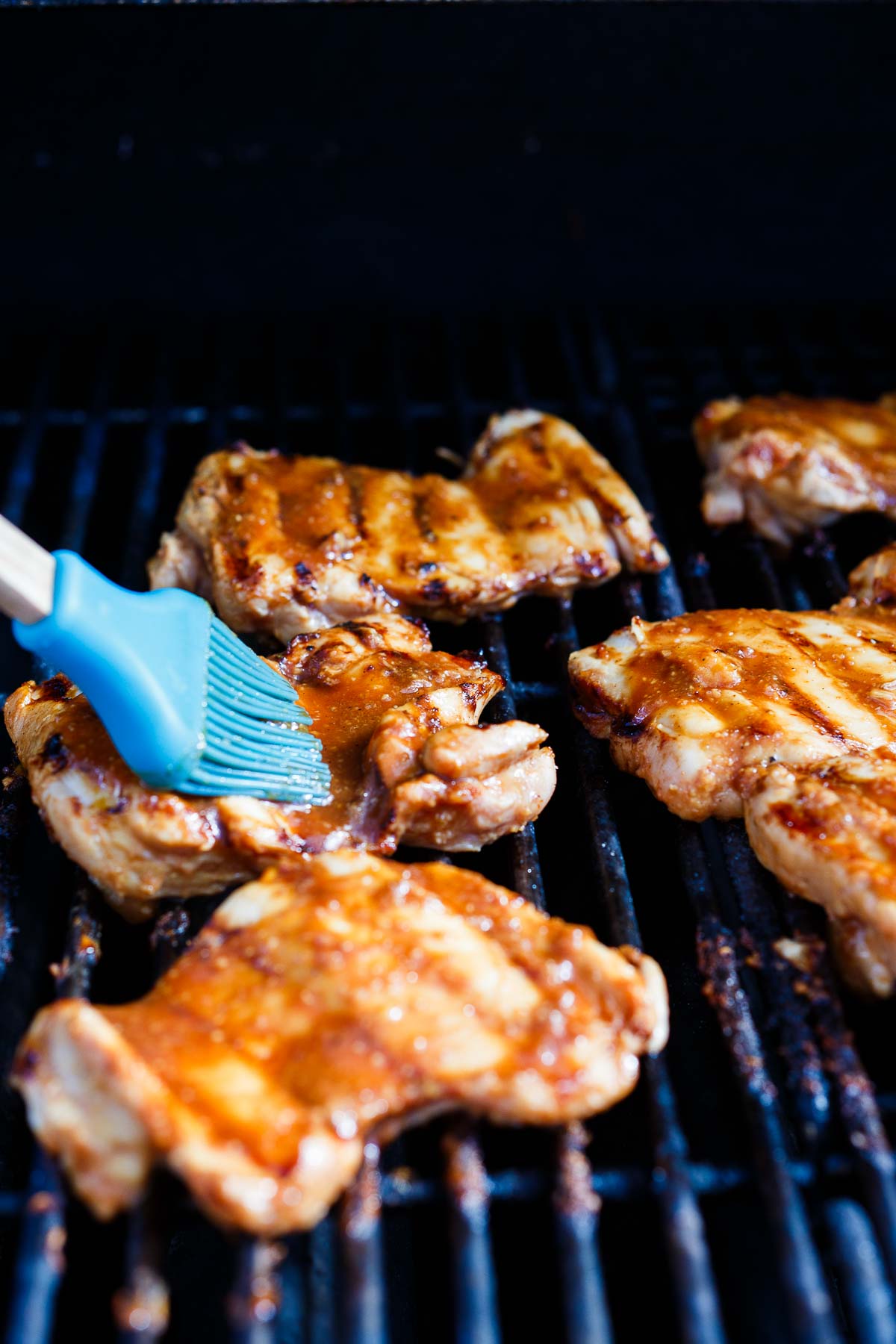 silicone brush brushing huli huli marinade over grilling chicken.