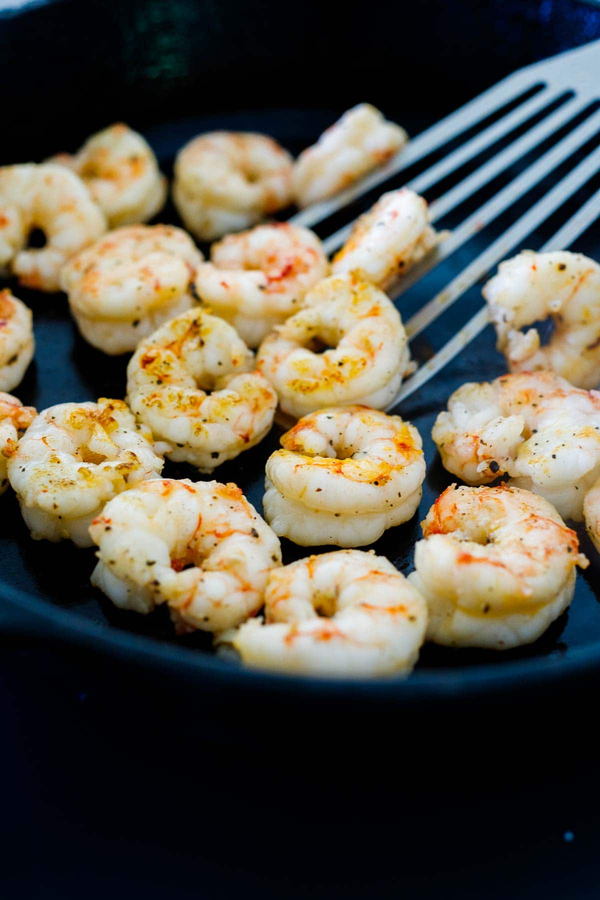 shrimp searing in skillet with metal spatula.