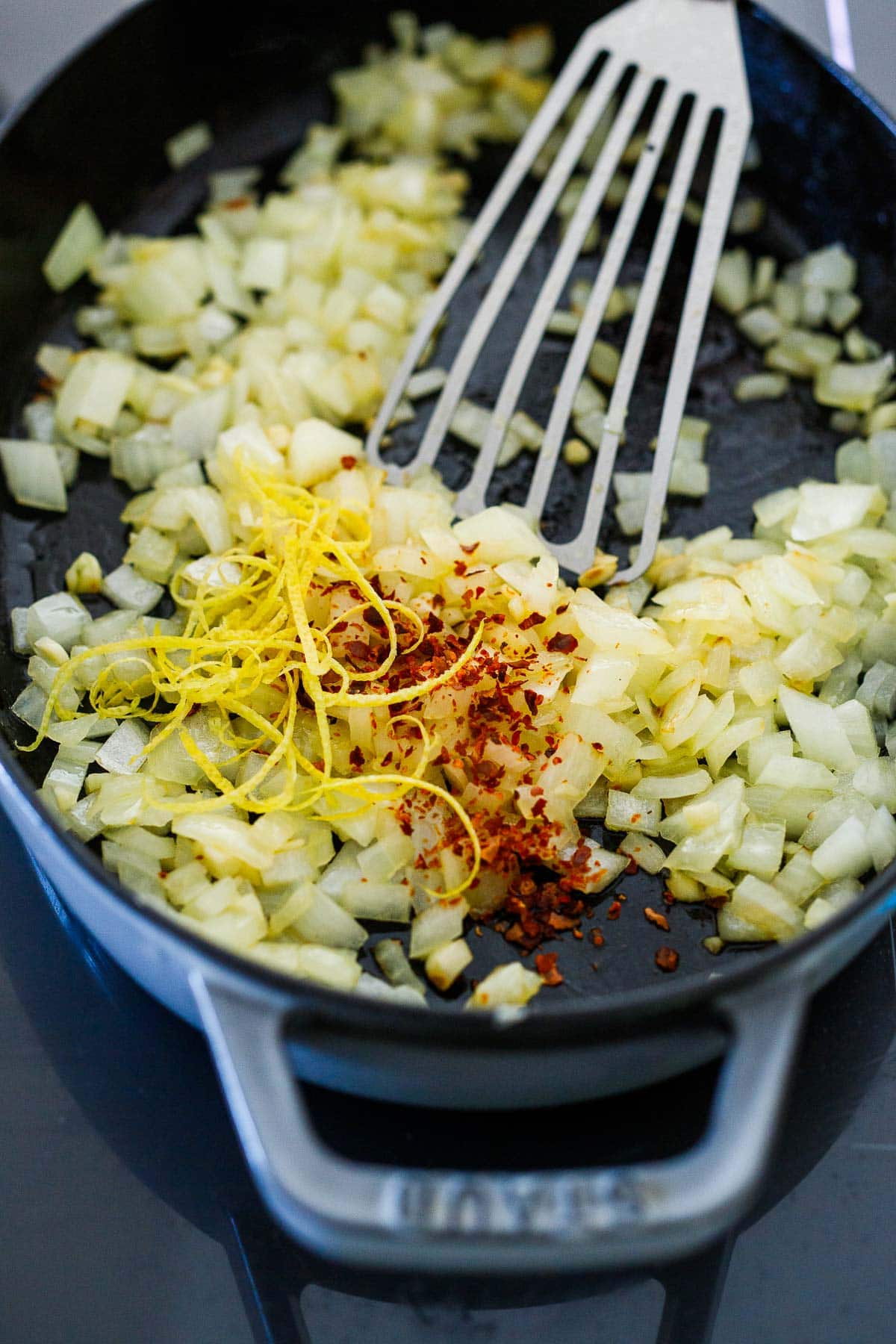 chopped onions sauteing in skillet with chili flakes and lemon zest.