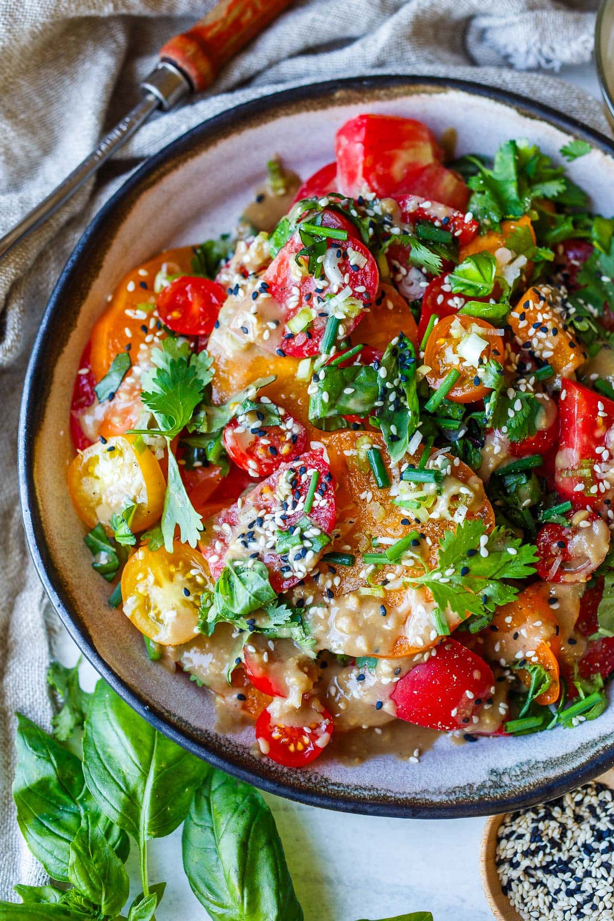 serving bowl with sliced heirloom tomatoes topped with sesame ginger dressing, toasted sesame seeds, and fresh herbs. 