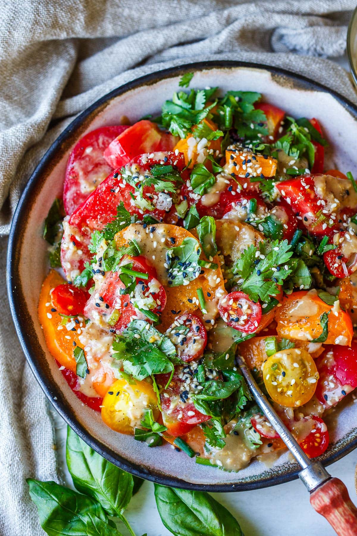 serving bowl with sesame tomato salad topped with sesame ginger dressing, toasted sesame seeds, and herbs. 
