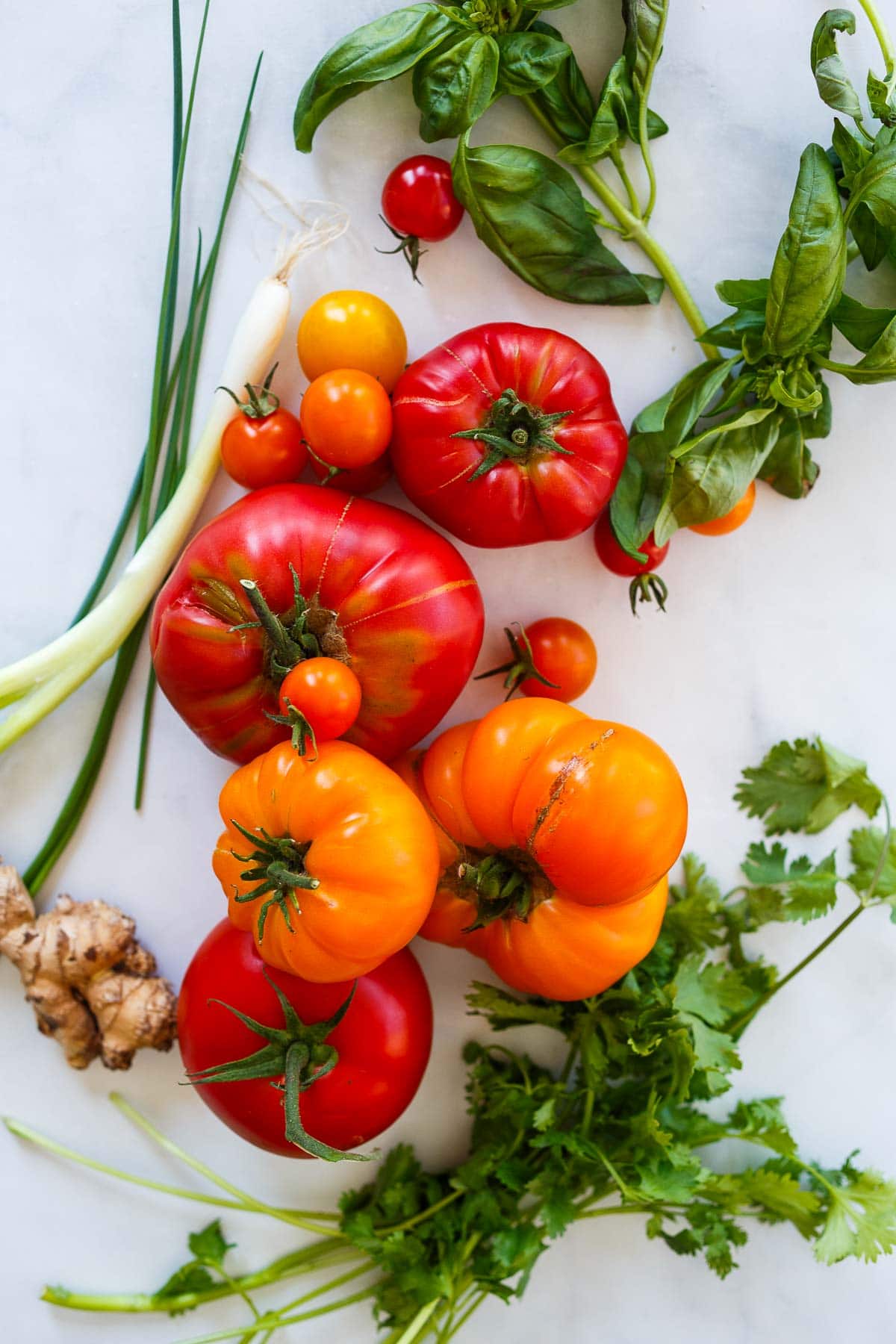 ingredients laid out for sesame tomato salad - heirloom tomatoes and cherry tomatoes, fresh herbs, and ginger. 