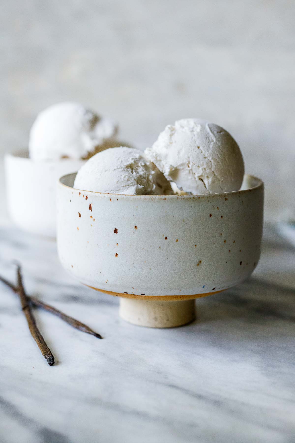 ceramic bowl with dairy-free ice cream scoops next to vanilla bean threads. 