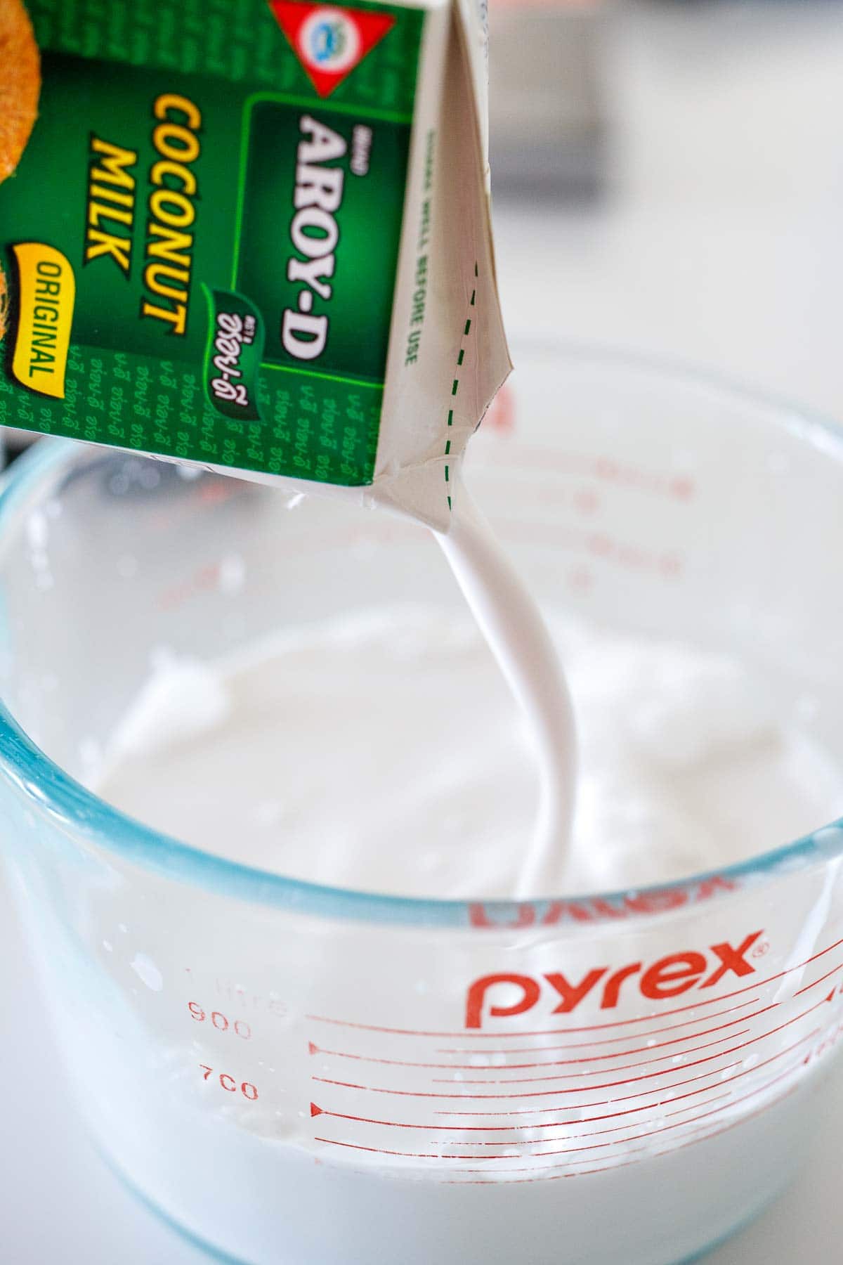 pouring box of coconut milk into glass 4-cup measuring cup.