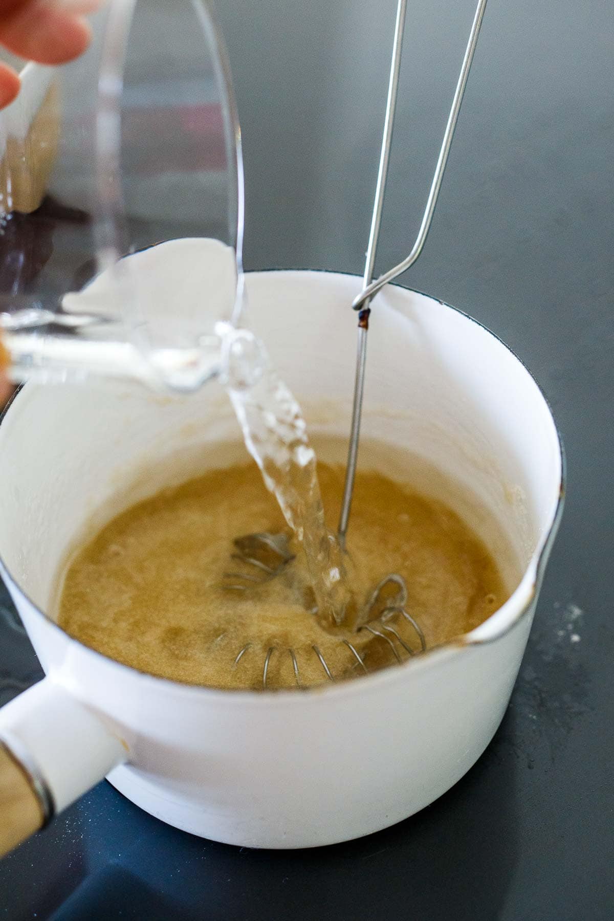 pouring water into saucepan with sugar and whisk.