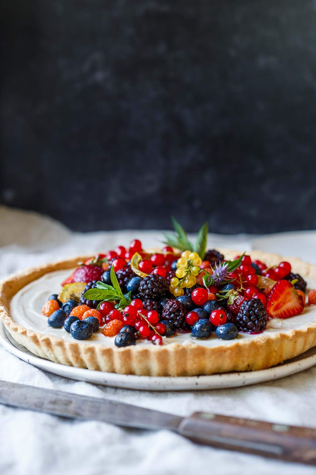 vegan berry tart on plate garnished with colorful array of different berries and herbs piled high.