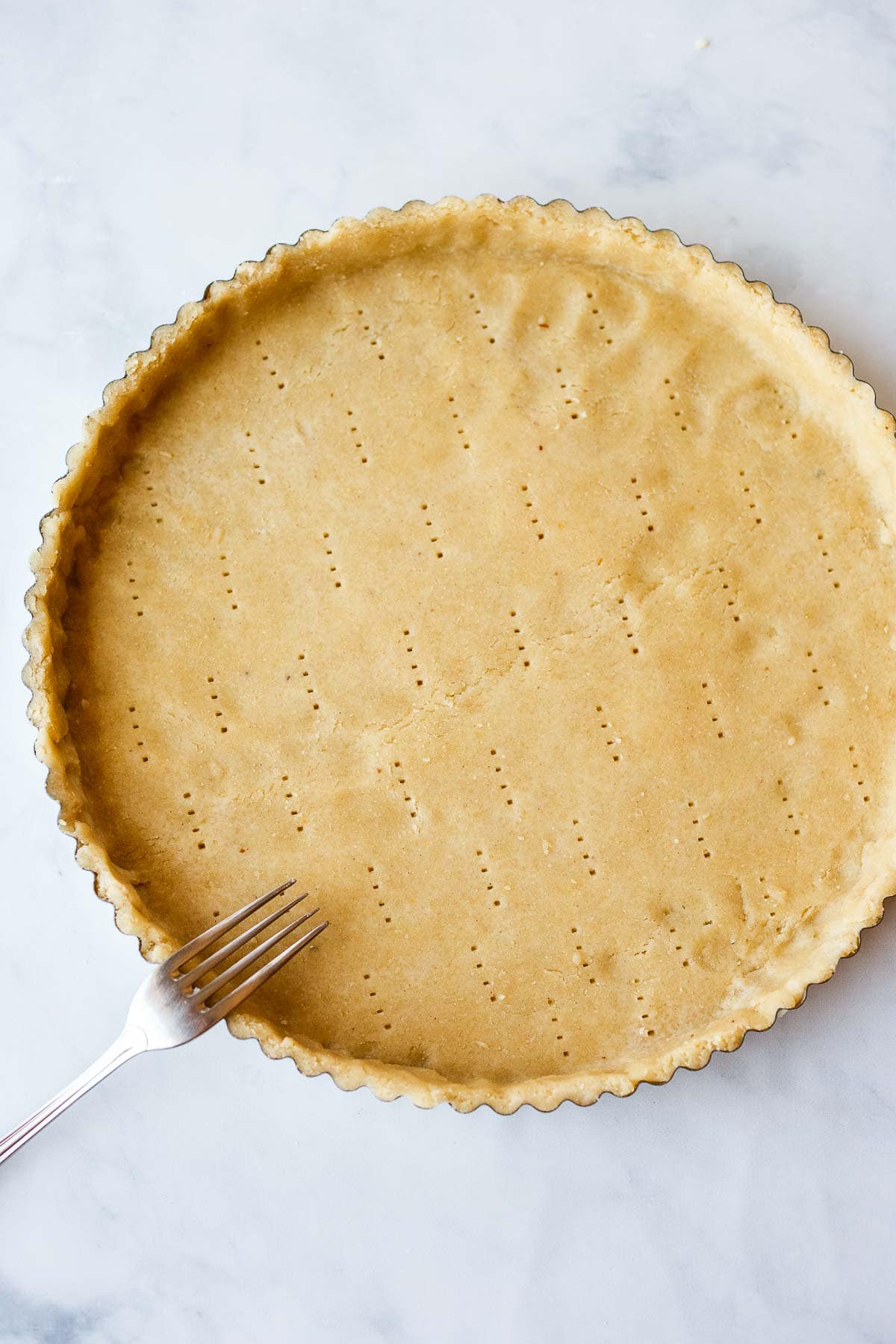 tart pan with unbaked dough formed into pan with fork marks.