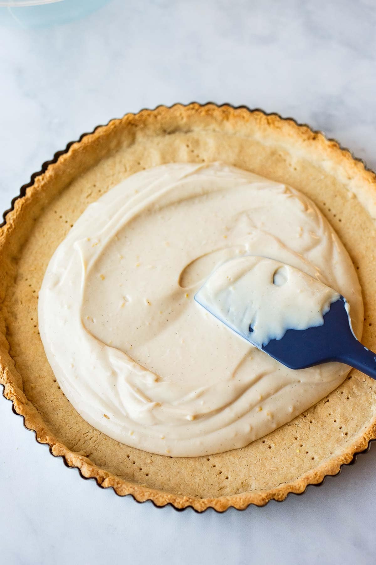 silicone spatula spreading out vegan tart filling into tart crust.