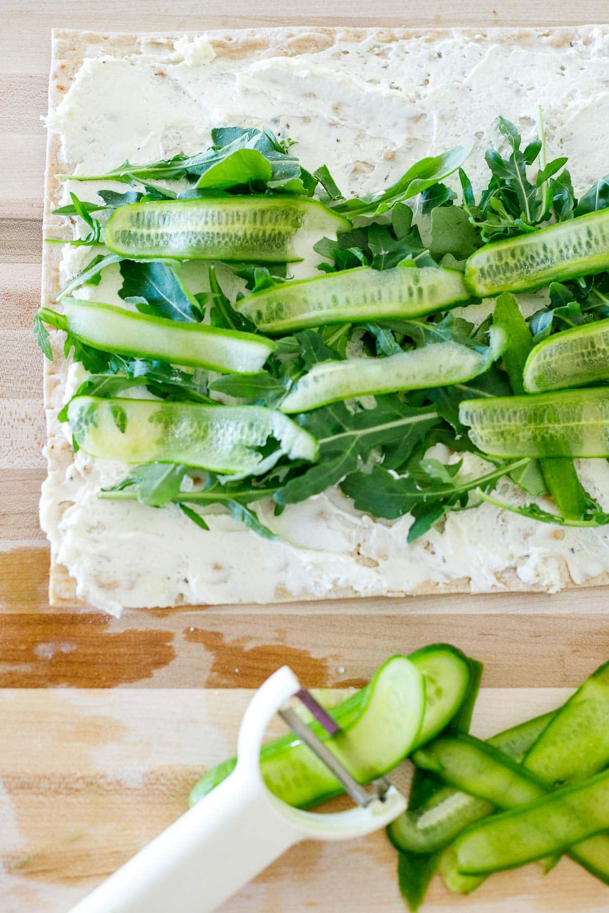 lavash bread with cream cheese topped with arugula and sliced cucumbers. 