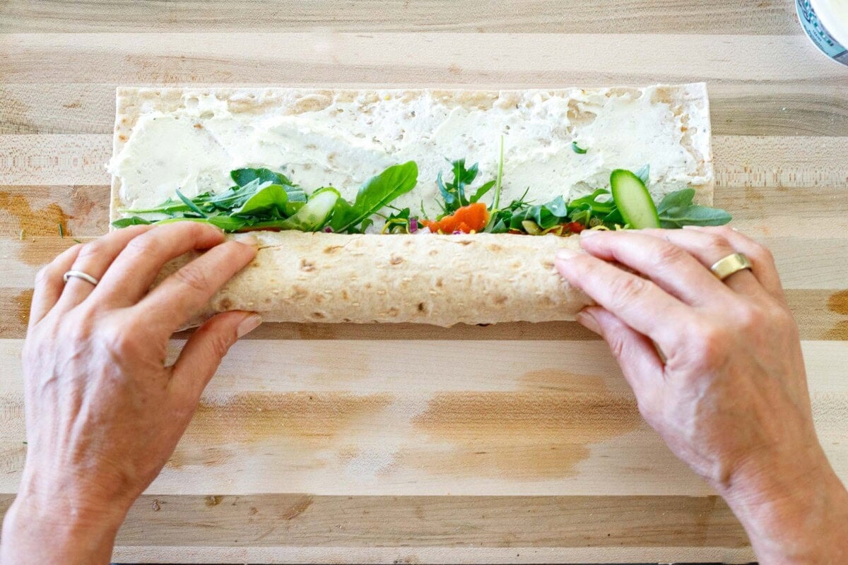 hands rolling lavash wrap with cream cheese and greens. 