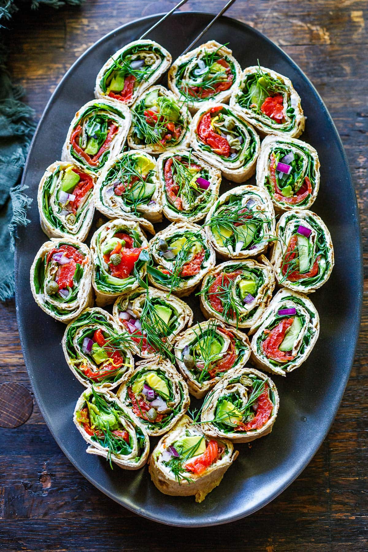 serving platter with sliced lavash wraps filled with smoked salmon, avocado, greens, red onion, and fresh dill. 