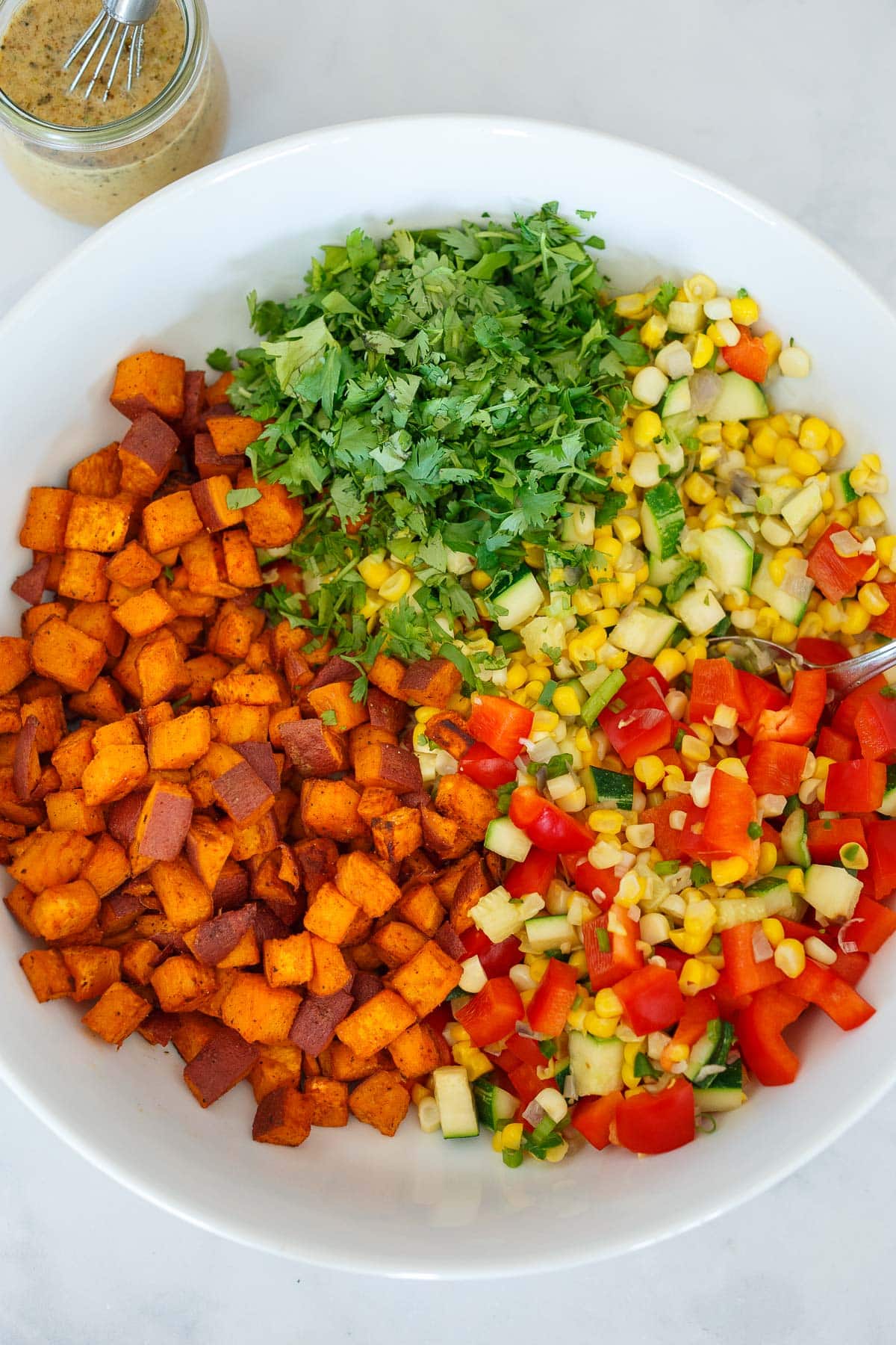 large salad bowl with roasted sweet potatoes, sautéed veggies, raw red bell peppers, and chopped cilantro. 