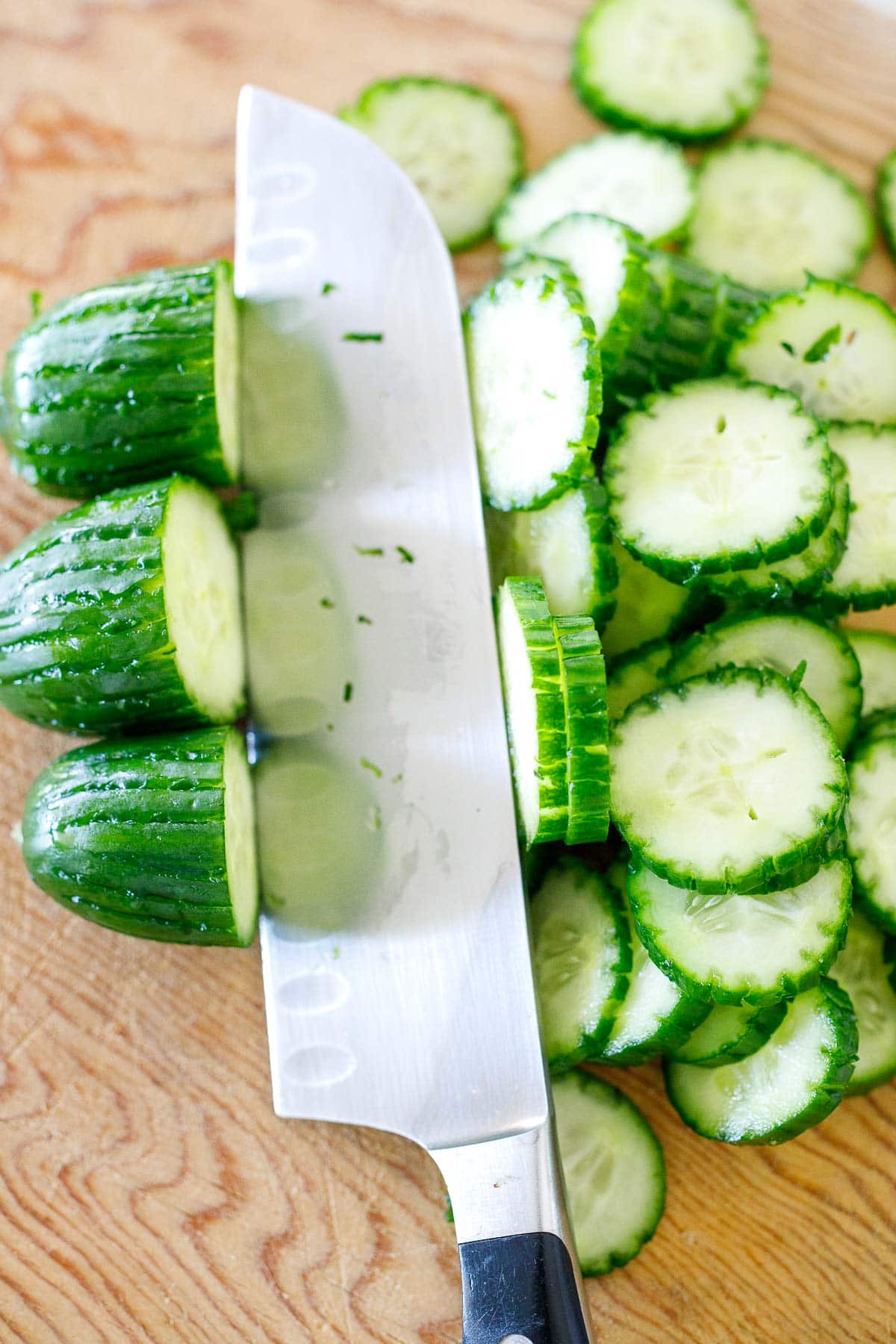 sharp knife slicing cucumbers on wood board. 
