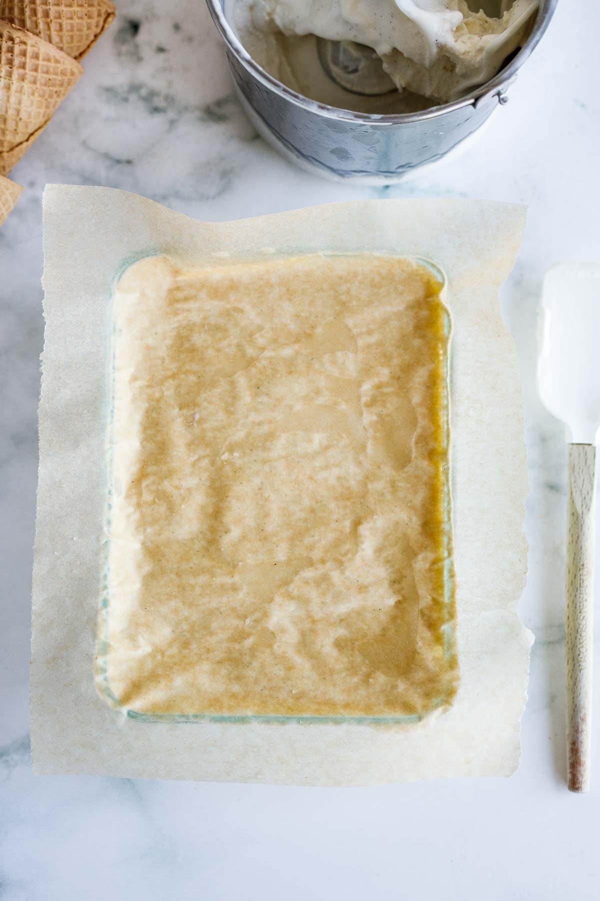 laying parchment on top of ice cream in rectangular glass container.