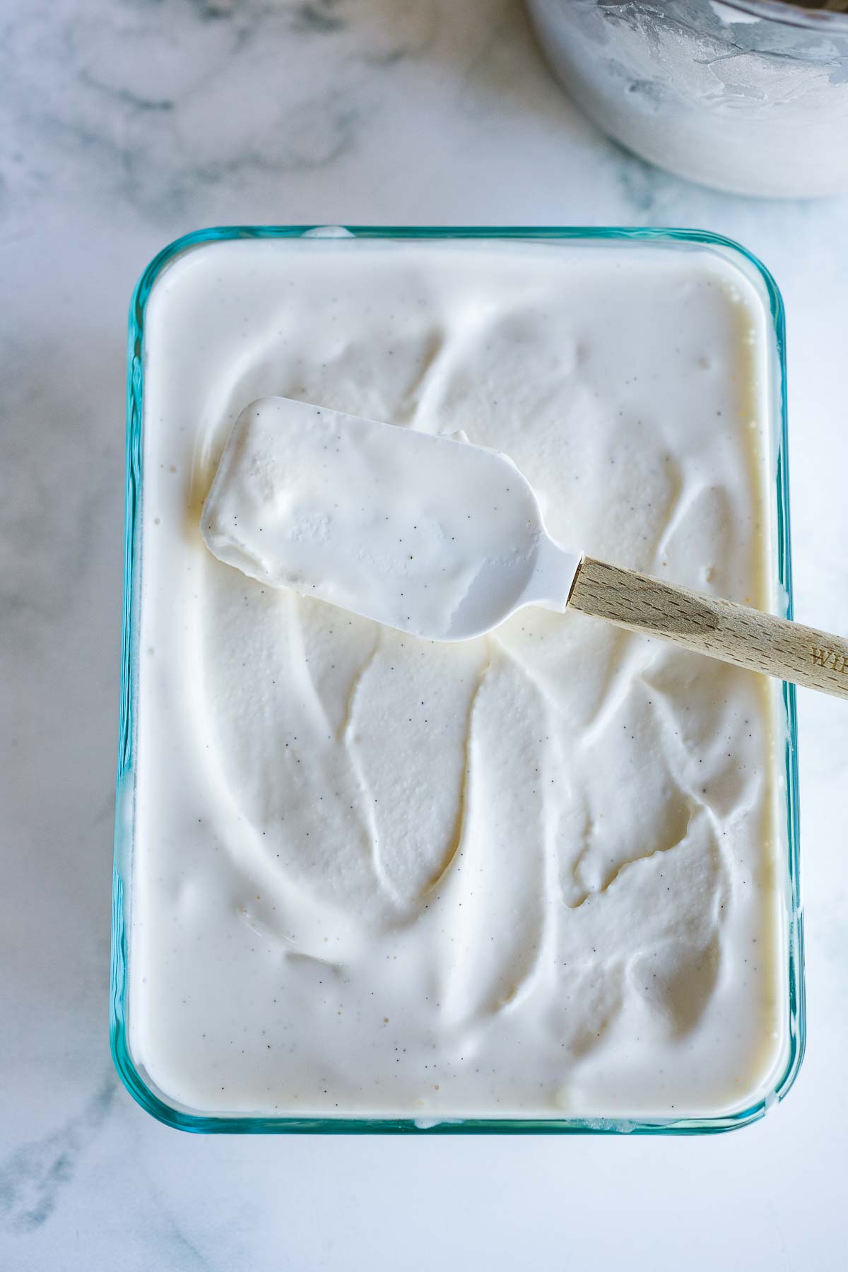 spatula spreading ice cream into rectangular glass container.