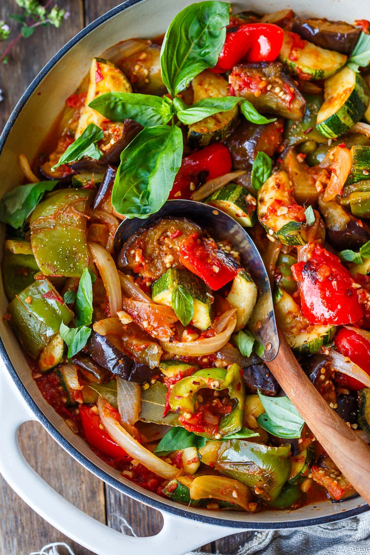 pot with cooked ratatouille served with fresh basil and serving spoon.