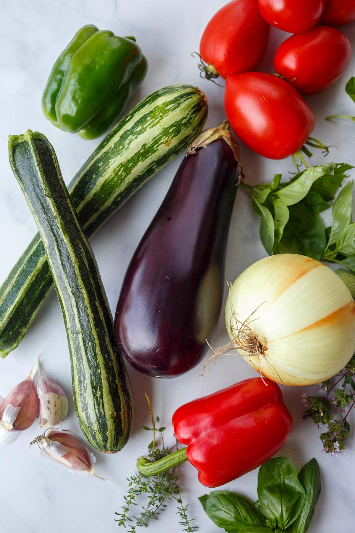 ingredients laid out for ratatouille - tomato, pepper, zucchini, eggplant, basil, onion, garlic, thyme. 