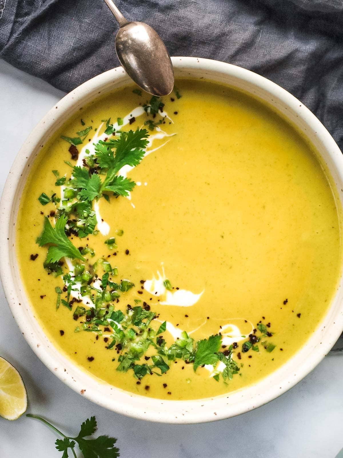 bowl of curried zucchini soup garnished with yogurt and fresh mint and cilantro. 