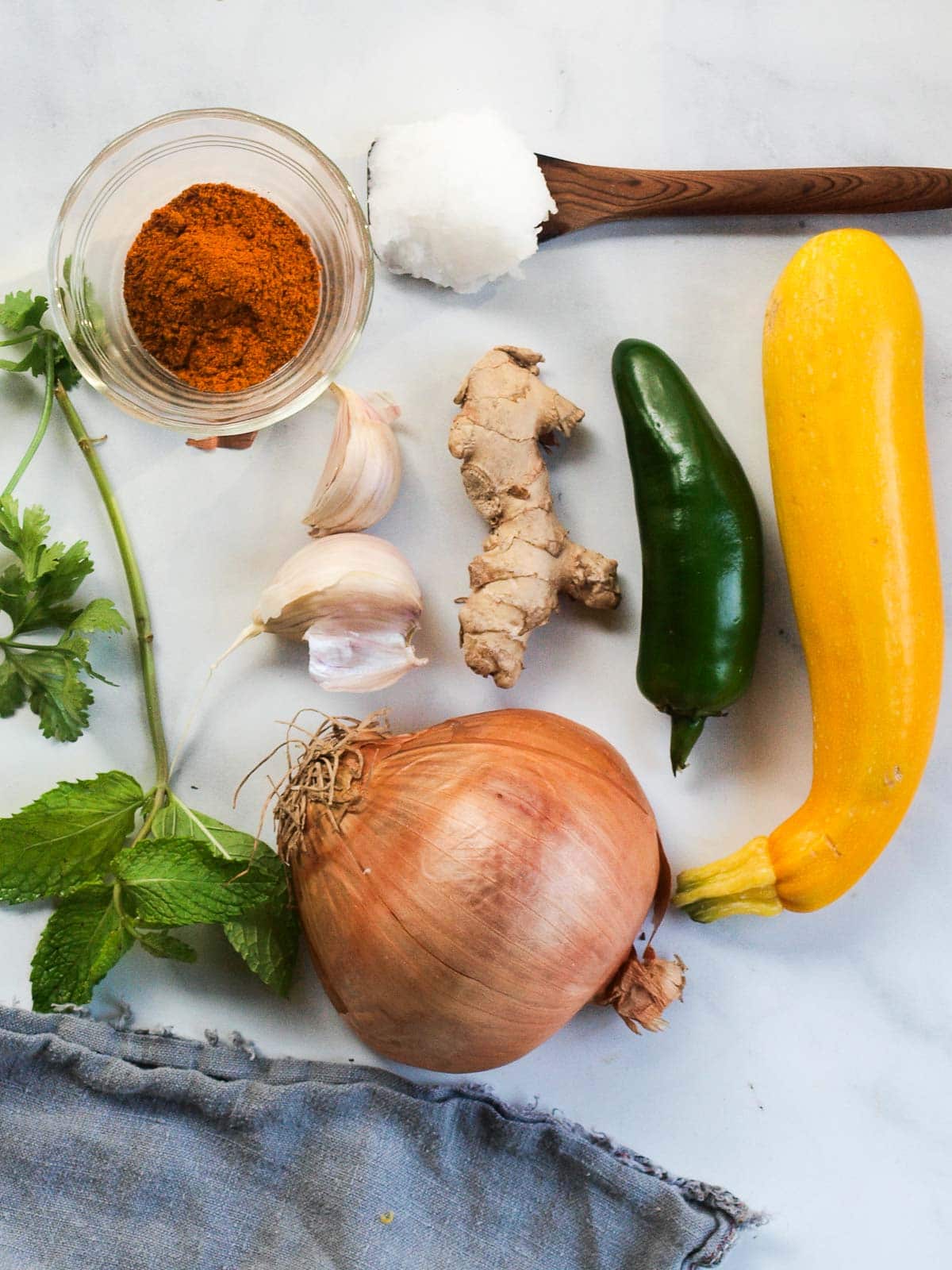 curried zucchini soup ingredients - herbs, curry powder, garlic, ginger, coconut oil, jalapeño, summer squash, yellow onion. 