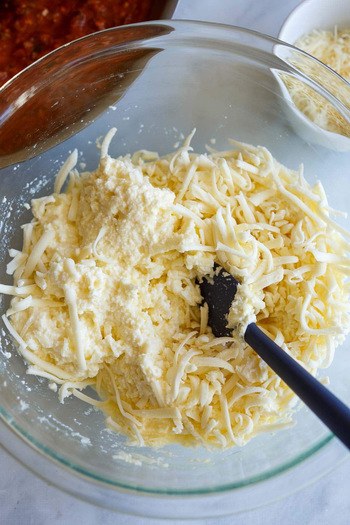 glass mixing bowl with ricotta cheese mixture and spatula.