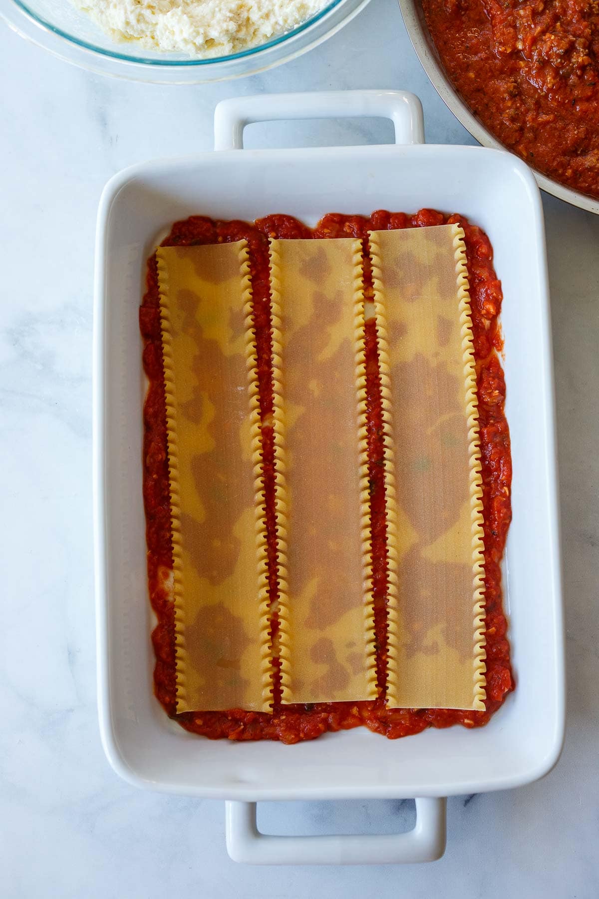 rectangular baking dish with layer of lasagna noodles placed on top of marinara sauce.