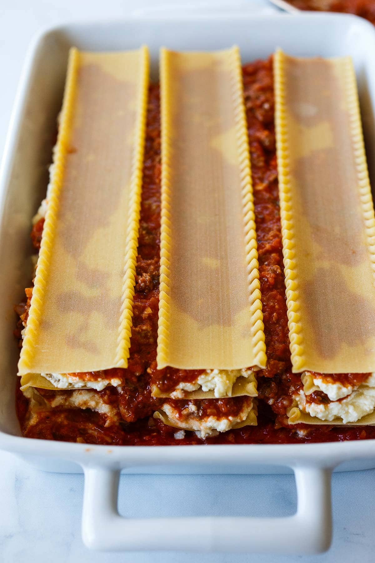 baking dish with layers of lasagna - sauce, noodles, ricotta cheese mixture, meat sauce, and lasagna noodles on top.