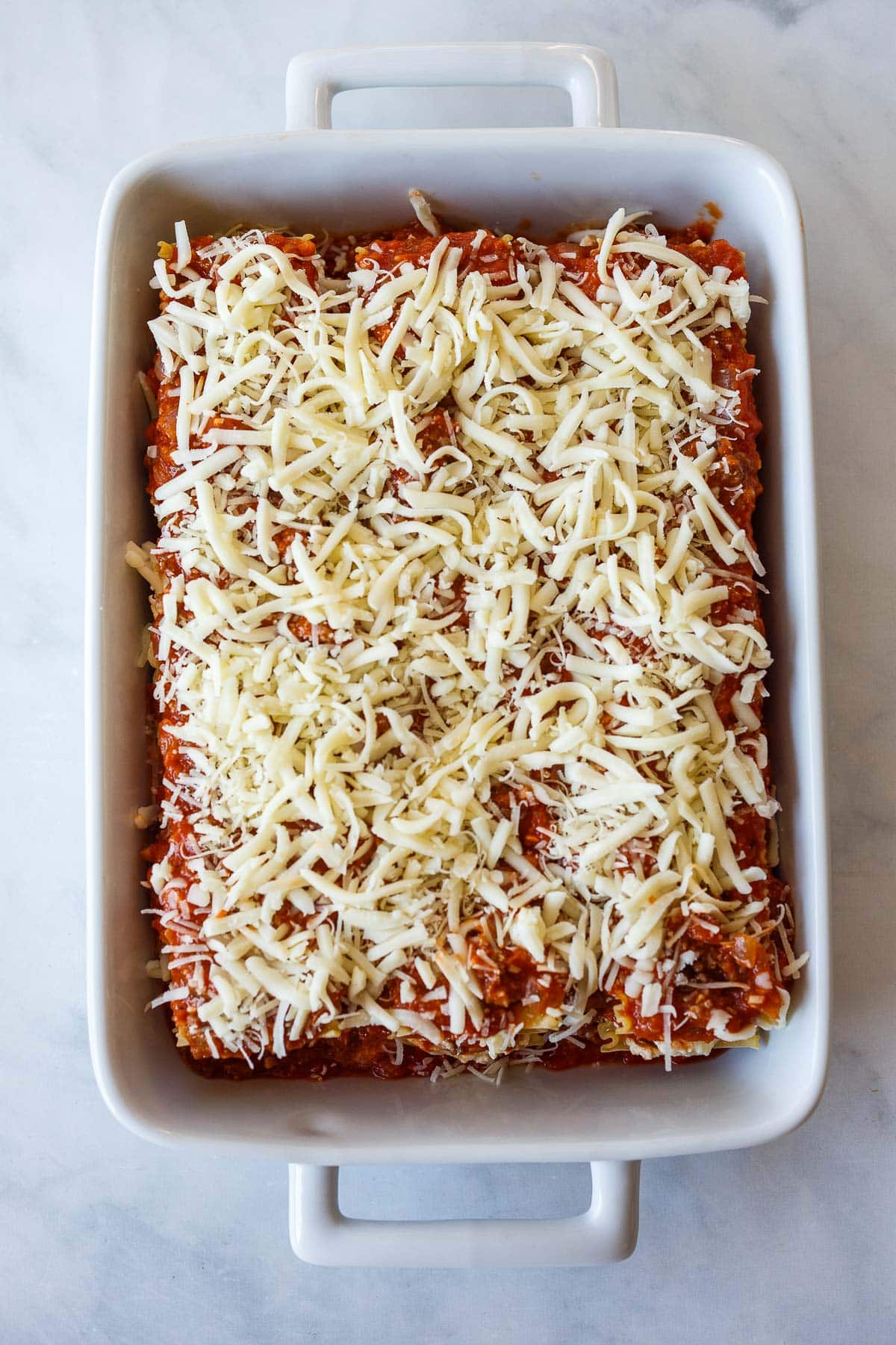 baking dish with unbaked lasagna topped with mozzarella and parmesan cheese.