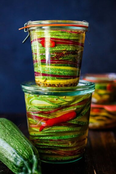 Zucchini pickles are delicious in sandwiches, burgers, or even just for snacking!  Easy to make and full of great flavor, this recipe makes great use of your late-summer harvest, preserving them for weeks in the fridge! They make a beautiful hostess gift as well!