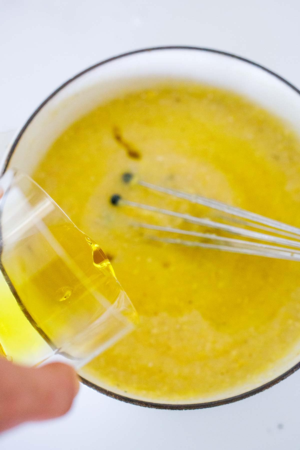 pot of cooked polenta with whisk and jar pouring oil into pot.