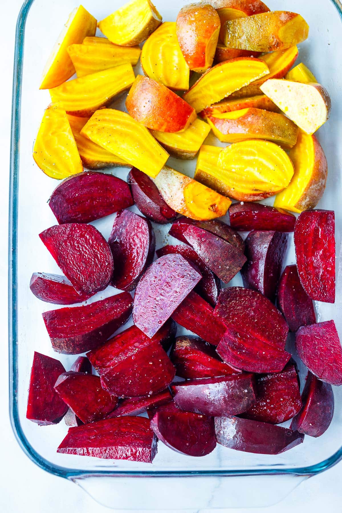 glass baking dish with red and gold beets cut into wedges seasoned in oil, salt, and pepper.