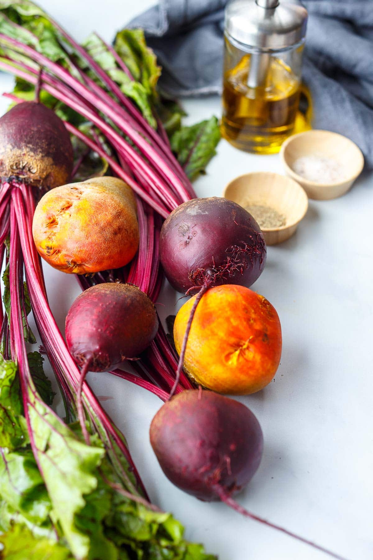 ingredients for roasted beets laid out - beets with their stems and greens, small dishes with black pepper and salt, and oil.