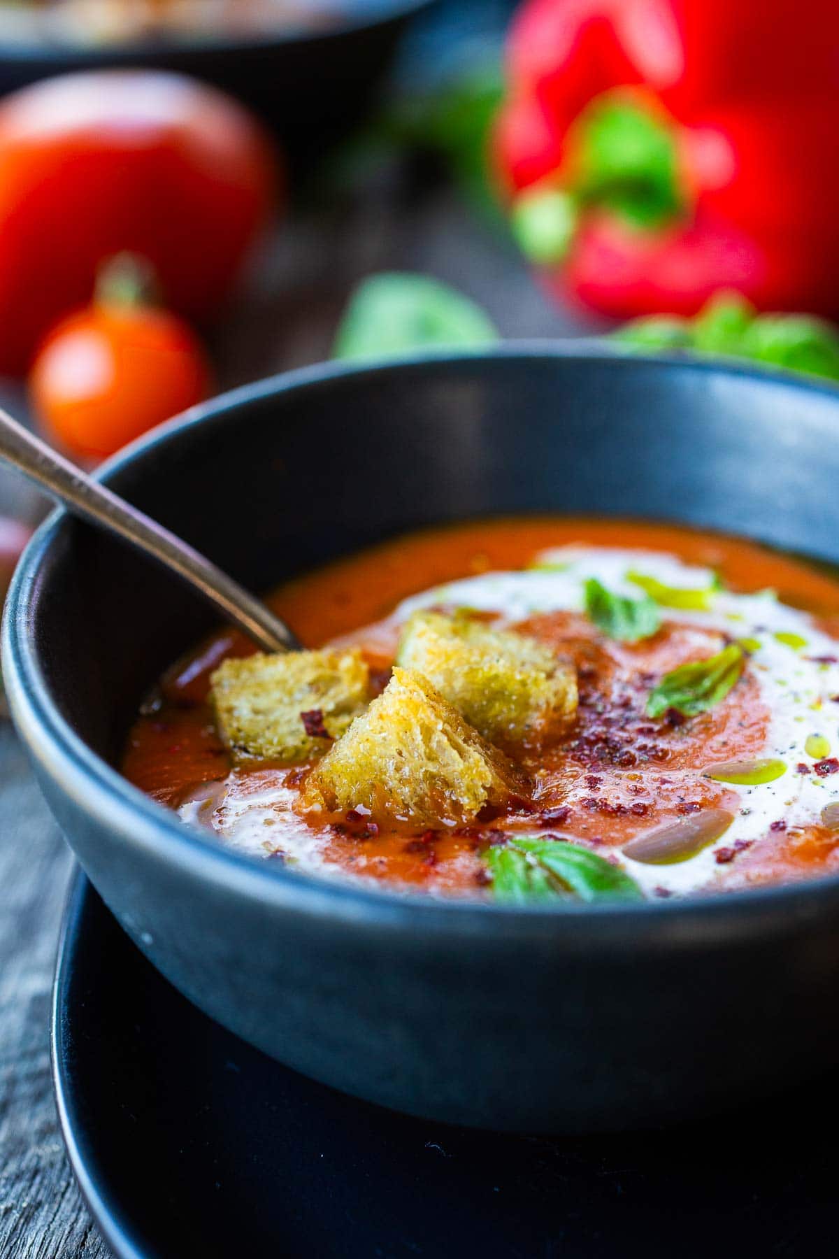 roasted red pepper tomato soup in bowl topped with croutons, basil, oil, and aleppo flakes. 
