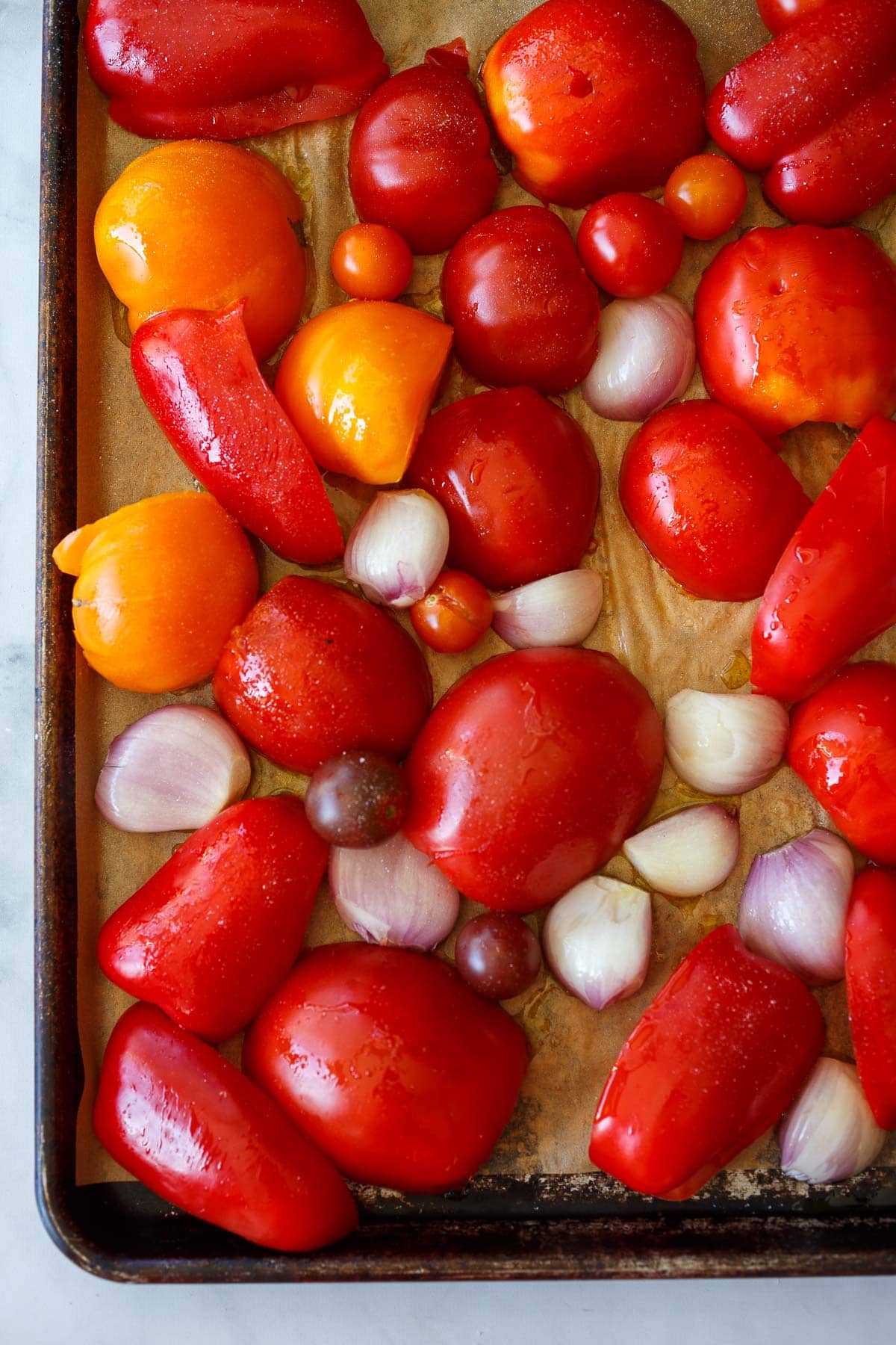 sheet pan with parchment and quarters of red bell peppers, tomato halves, and shallots laid out skin side up.