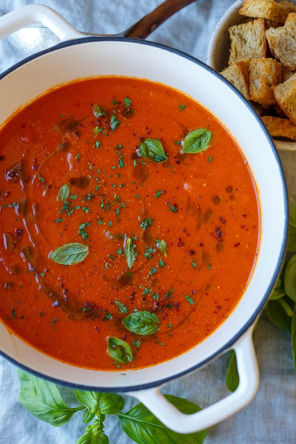 roasted red pepper tomato soup in pot garnished with olive oil and fresh herbs. 
