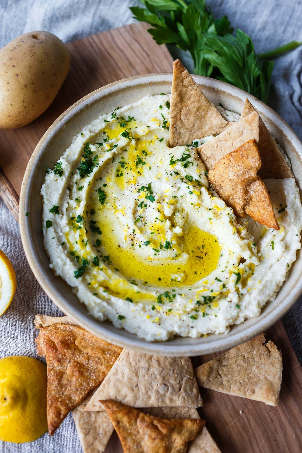 bowl of skordalia dip with drizzle of olive oil, fresh parsley, lemon zest, and pita chips. 