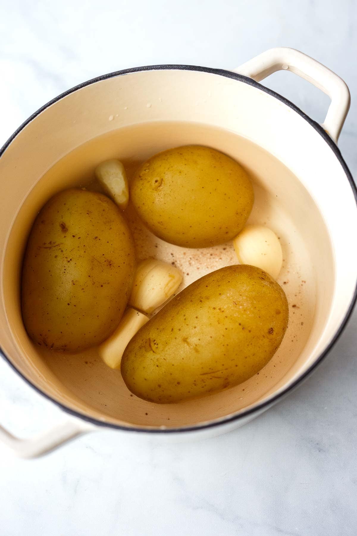 large pot with whole potatoes and garlic cloves in water. 