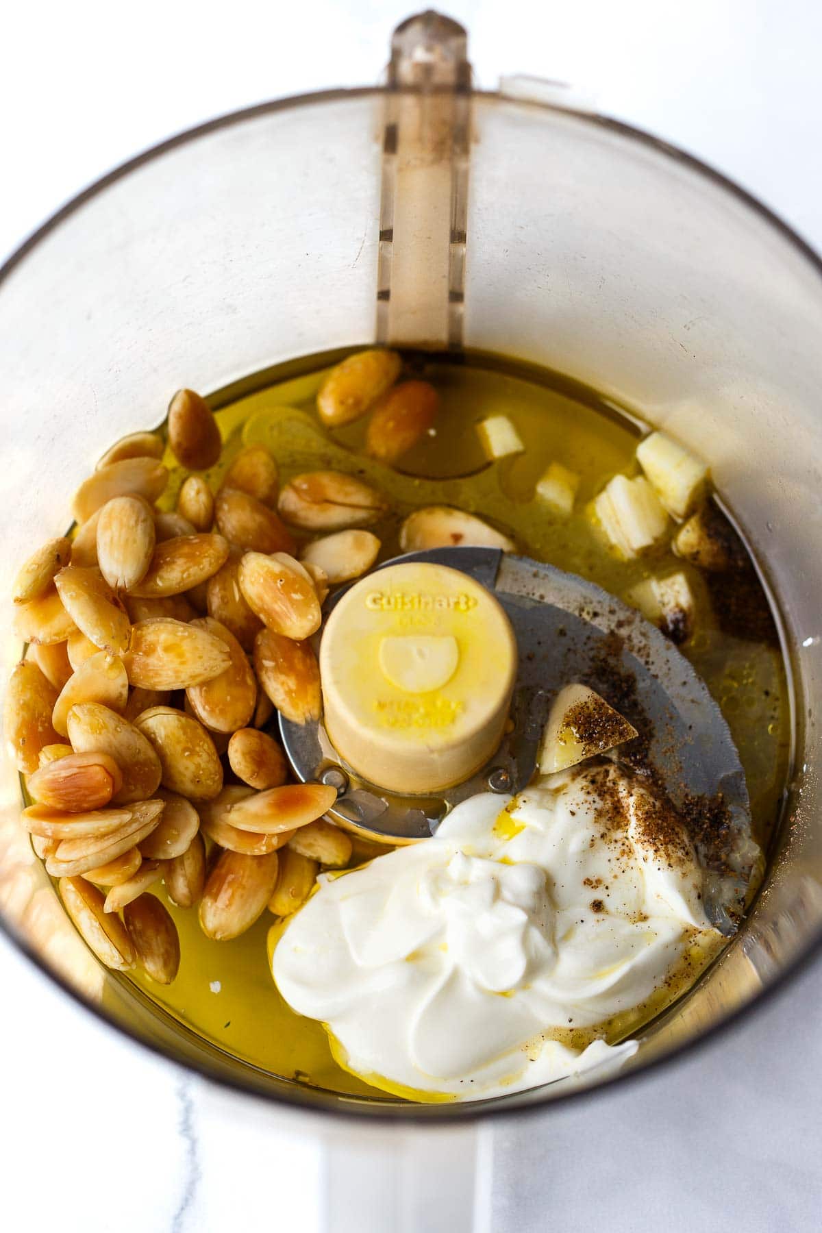 food processor with almonds, garlic, yogurt, and oil.