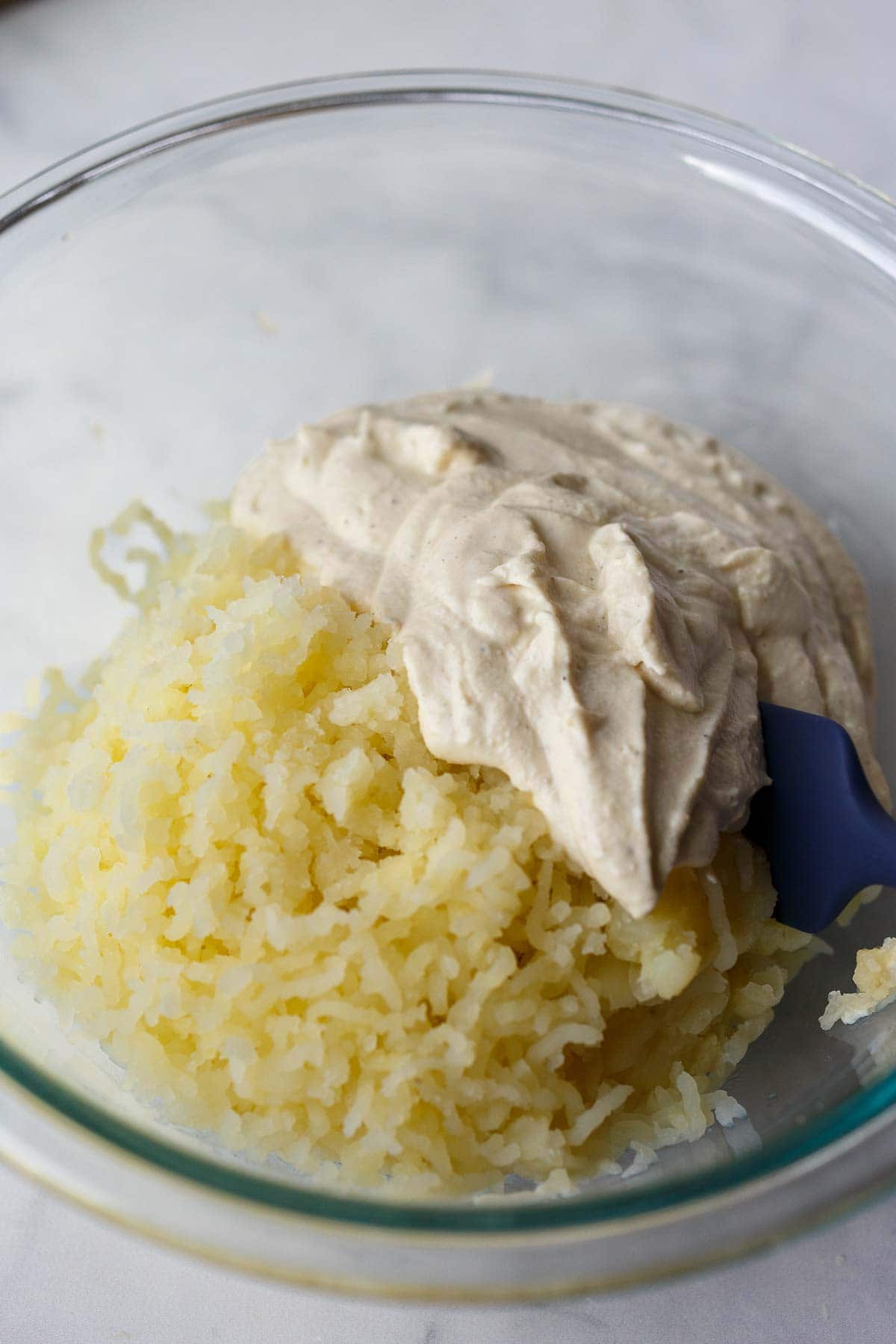 glass mixing bowl with riced potatoes and almond yogurt. 
