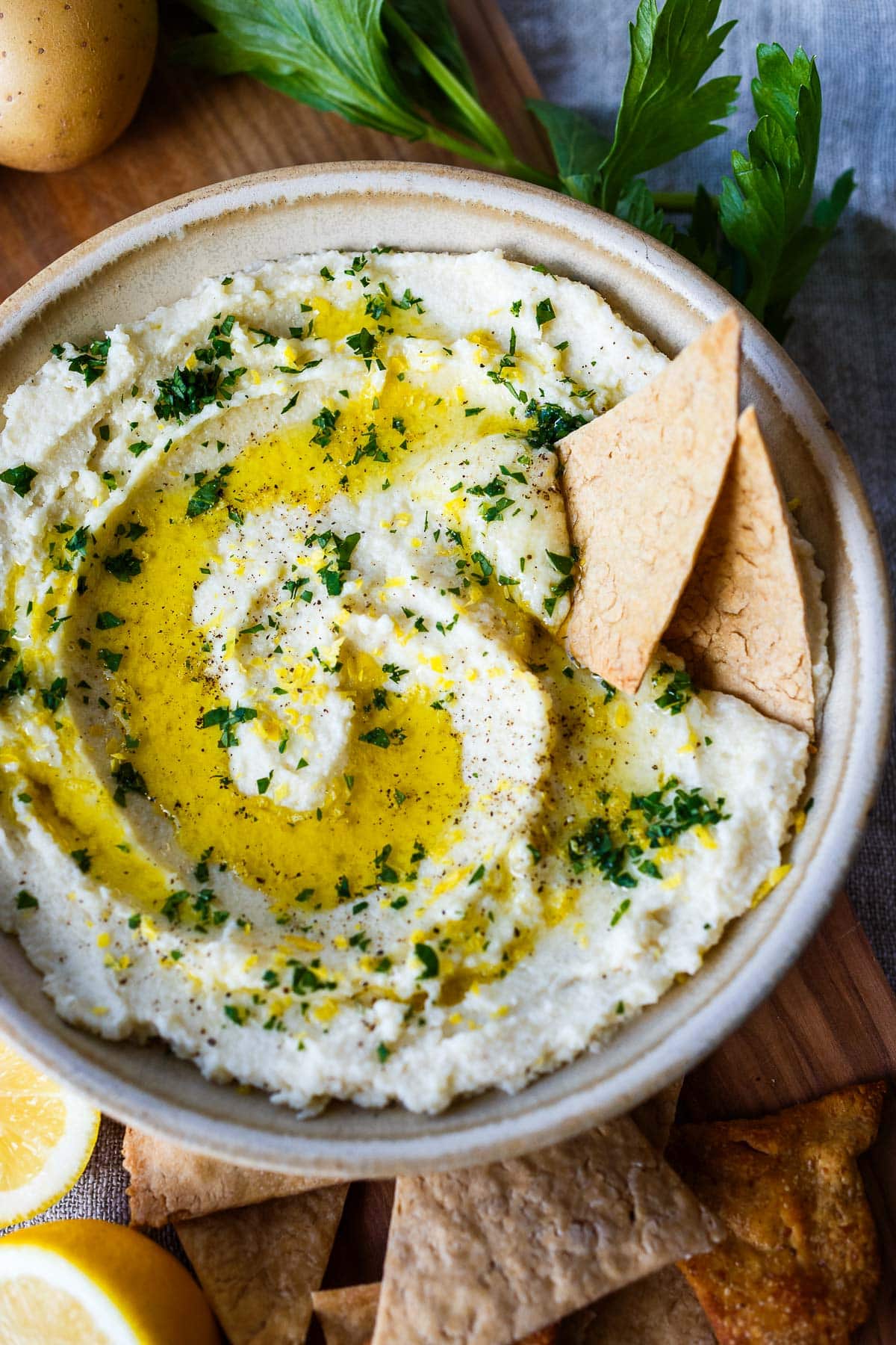 skordalia dip in serving bowl garnished with olive oil and minced parsley and lemon zest, with two pita crackers. 
