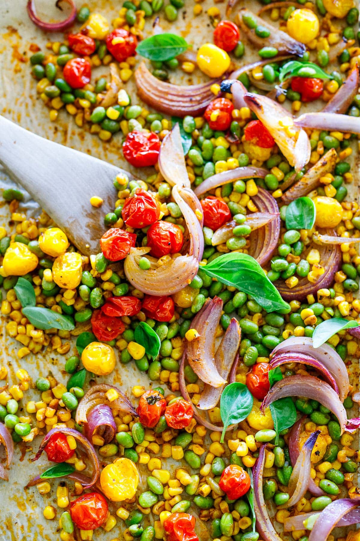 wood spatula mixing sheet-pan succotash on pan. 