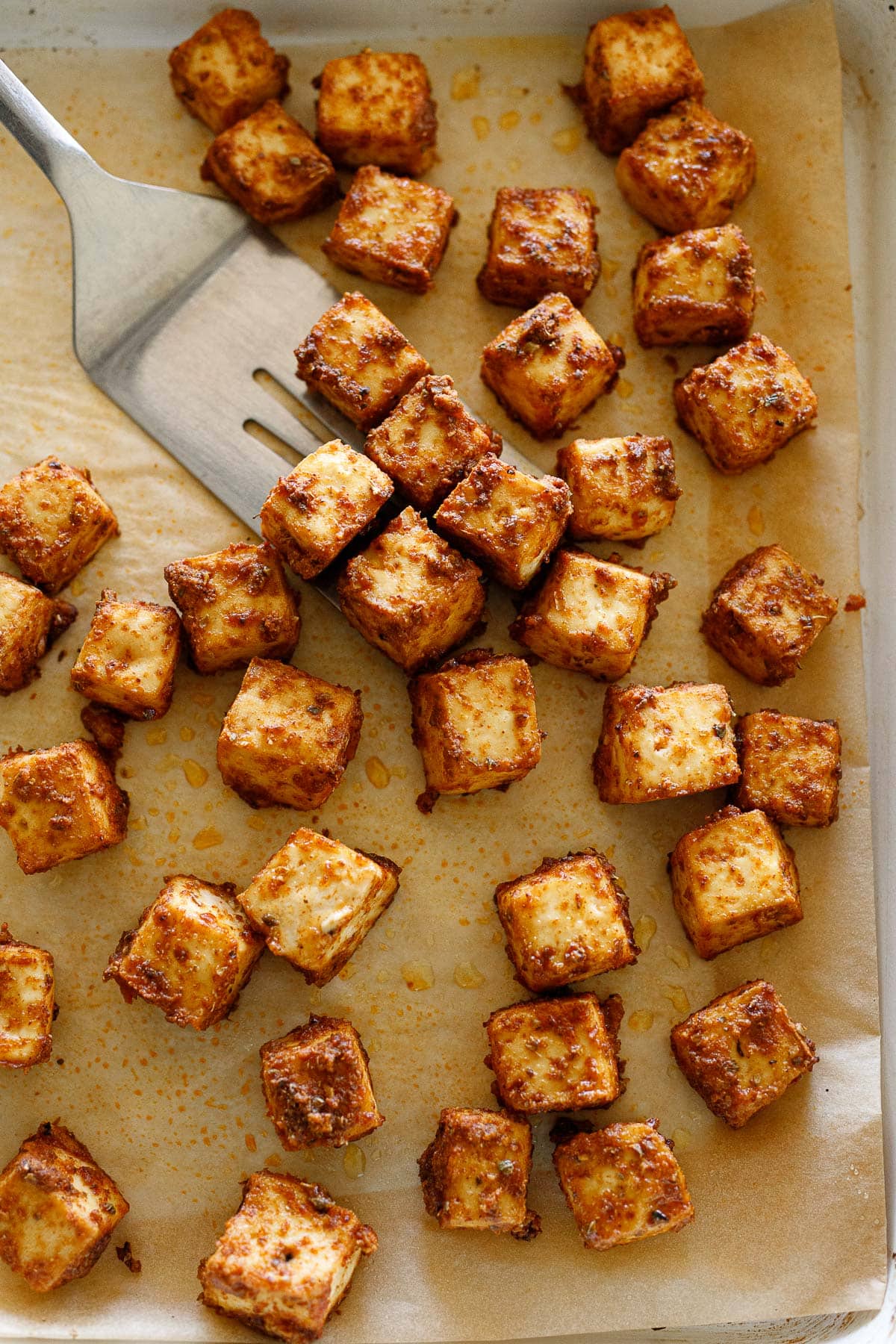 parchment lined sheet pan with baked tofu and spatula. 