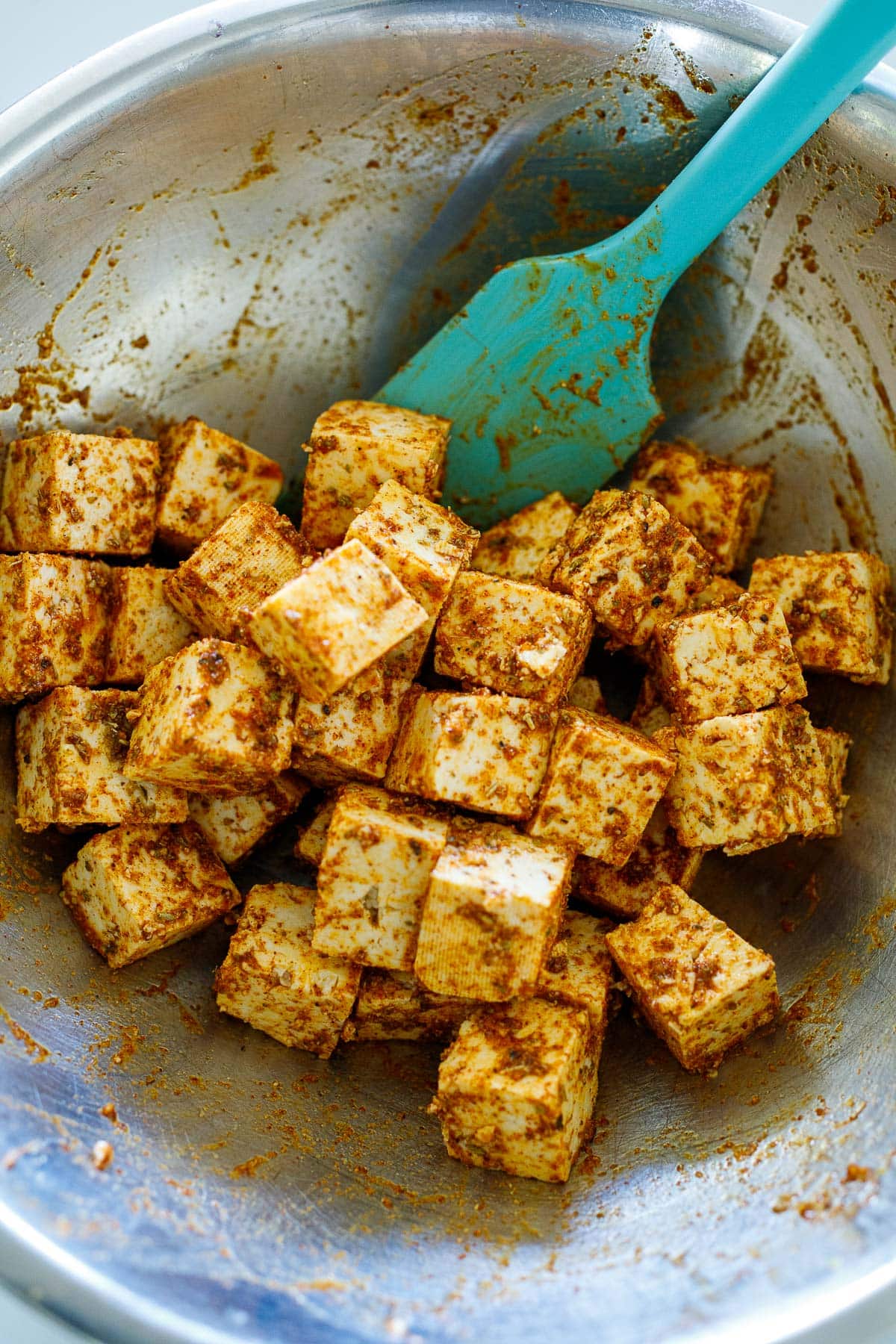 mixing bowl and spatula with seasoned cubed tofu.