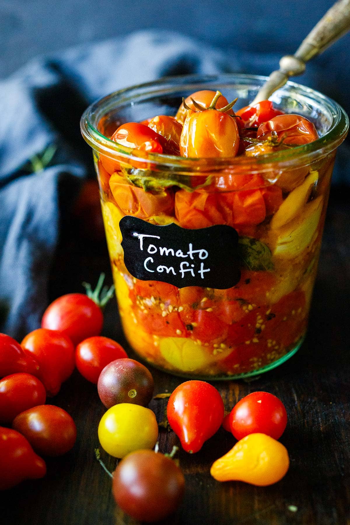 glass jar with the words "tomato confit" filled with tomato confit and basil.