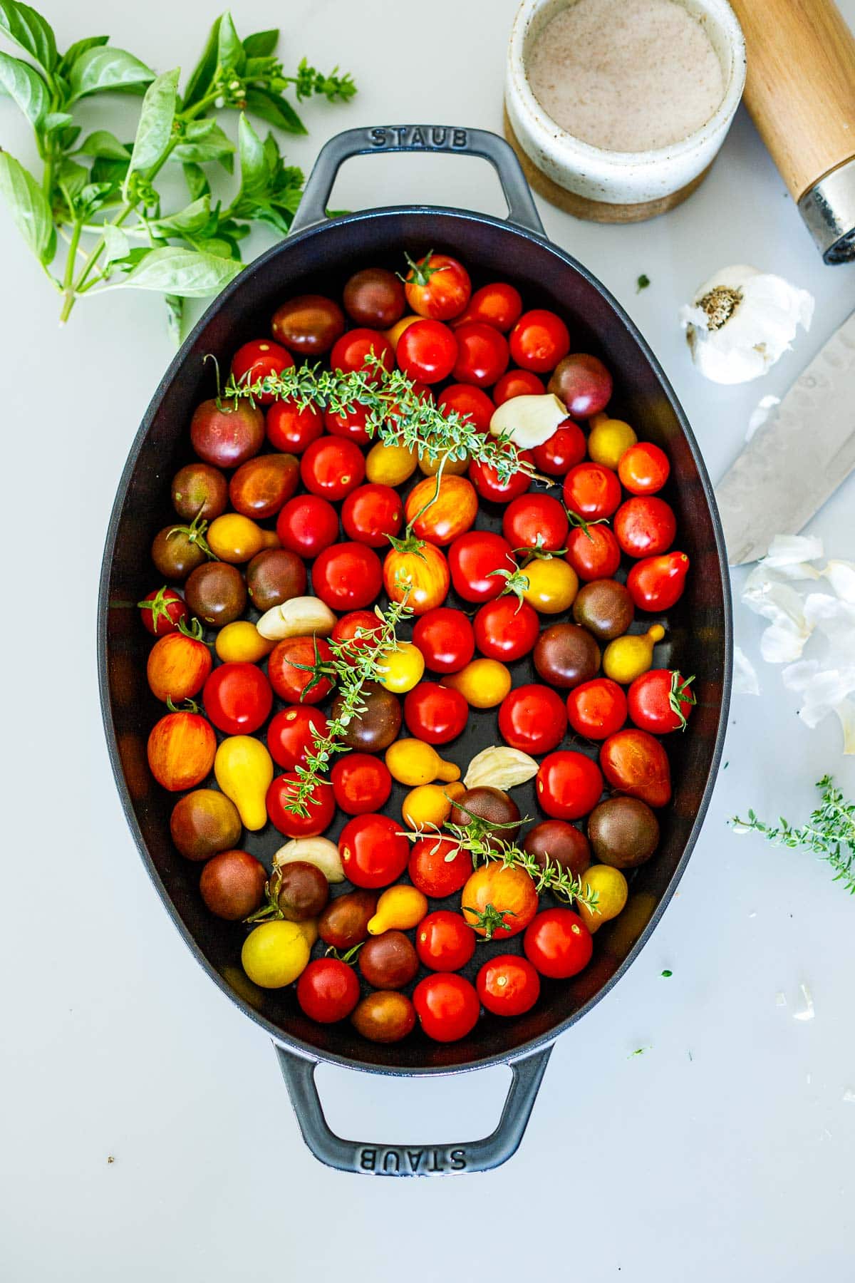 oval baking dish with fresh heirloom cherry tomatoes, garlic cloves, and thyme. 