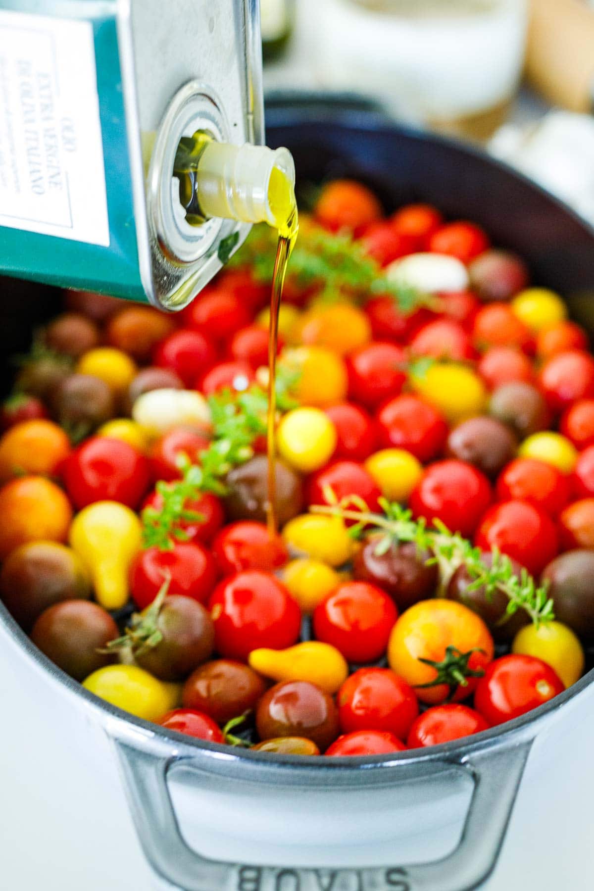 pouring olive oil into baking dish with cherry tomatoes and thyme. 