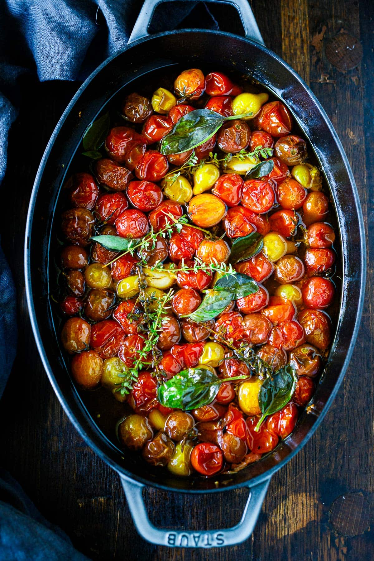 oval baking dish with tomato confit topped with thyme and basil.